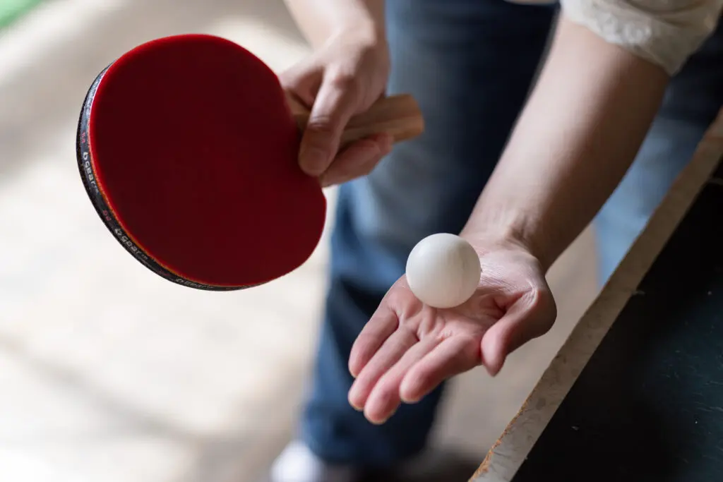 Person holding table tennis paddle and ball