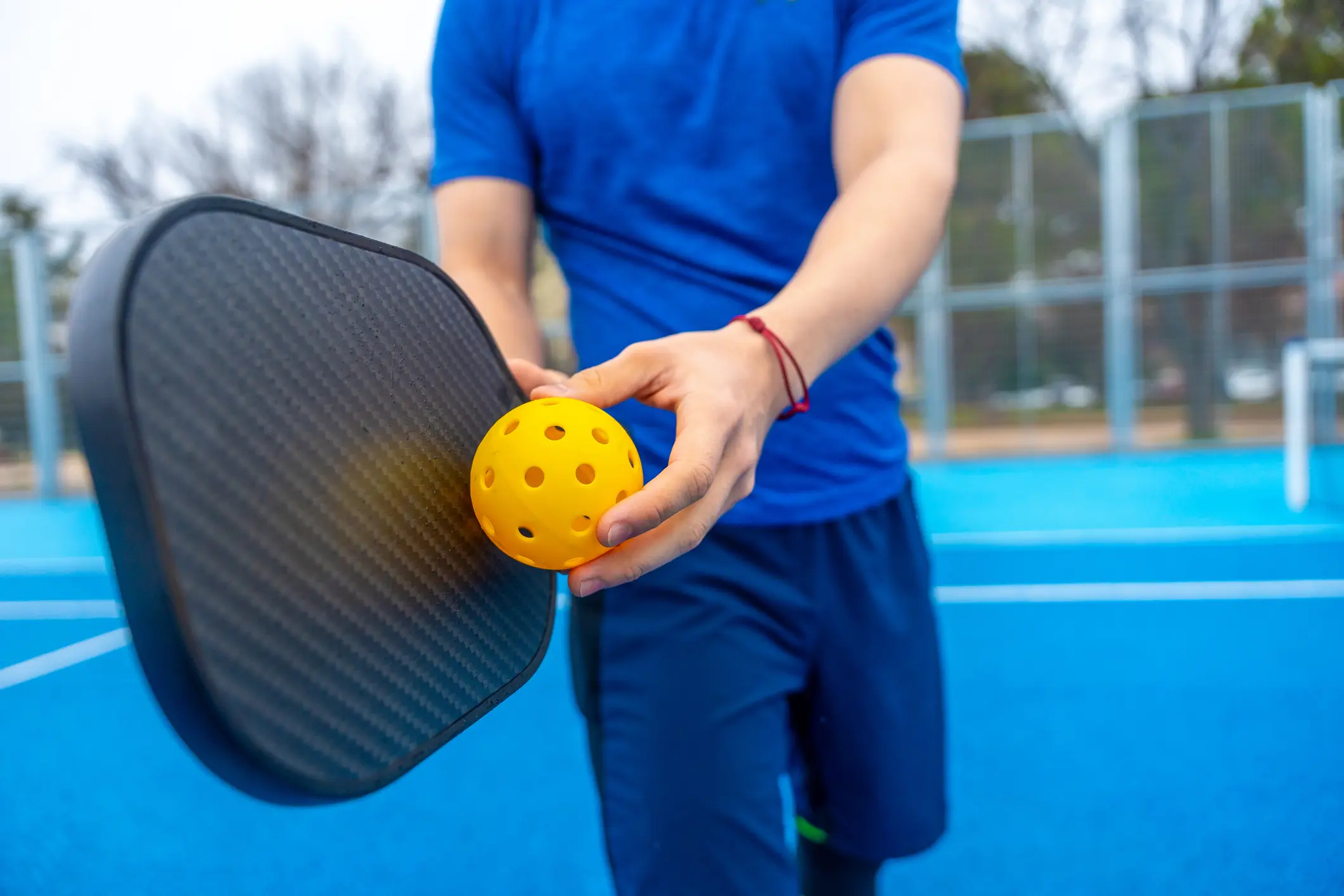 Person holding pickleball paddle and yellow ball