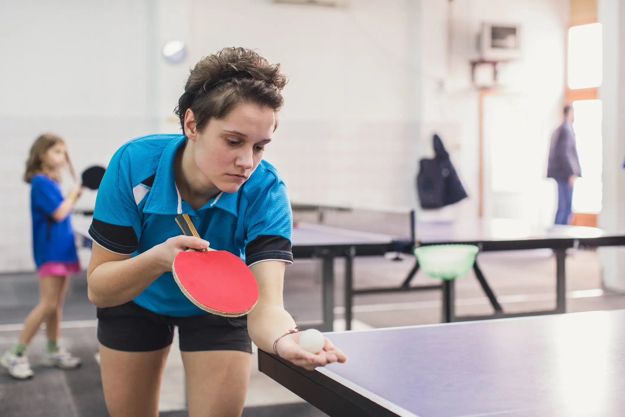 A woman engaged in a game of table tennis, smiling while playing with her friends in a lively setting.